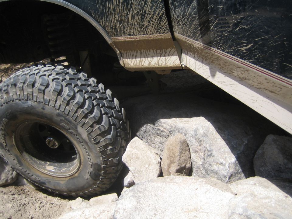 Close-up of a large knobby off-road tire wedged against rocks under a truck