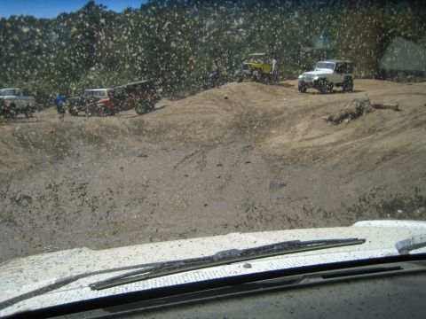 1990 Ford Bronco - Several Jeeps and 4x4s gather on a dusty hillside trail viewed through a heavily mud-spattered windshield with wipers.