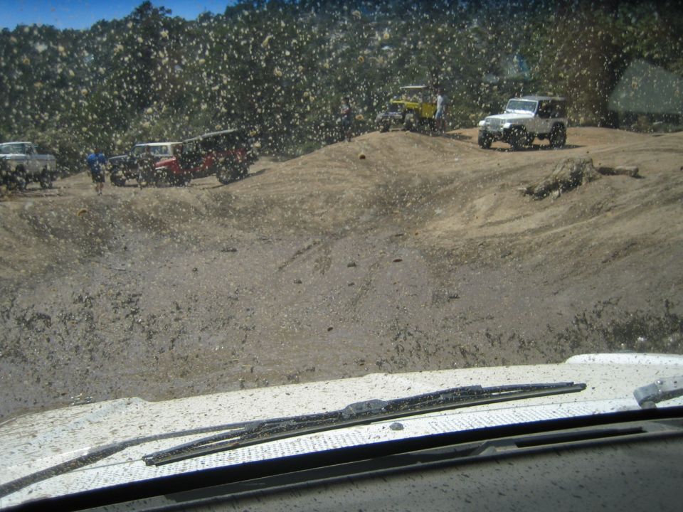 Several 4x4 vehicles parked on a dirt slope seen through a muddy windshield