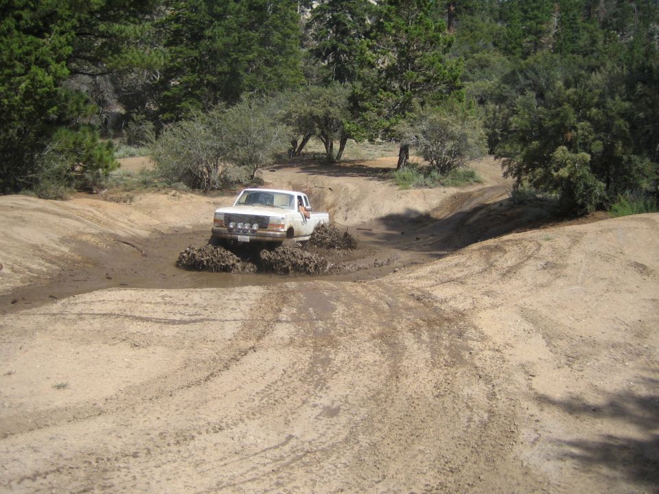 White pickup truck driving through a muddy water hole on a dirt trail