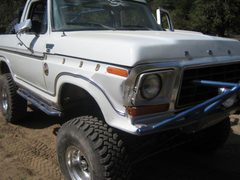 1990 Ford Bronco - Close-up of the front corner of a white Ford 4x4 truck showing chrome fender trim, round headlight and a blue tube bumper.