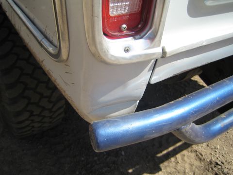 1990 Ford Bronco - Close-up of a dented and scratched white truck rear quarter panel with a red tail light and a blue steel tube rear bumper.