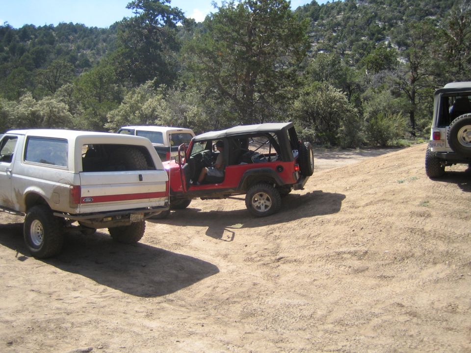 Red Jeep Wrangler with doors off parked beside a white Ford truck on dirt