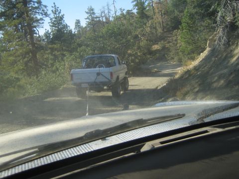 1990 Ford Bronco - View through a dusty windshield of a white lifted pickup truck climbing a steep dirt trail among pine trees.