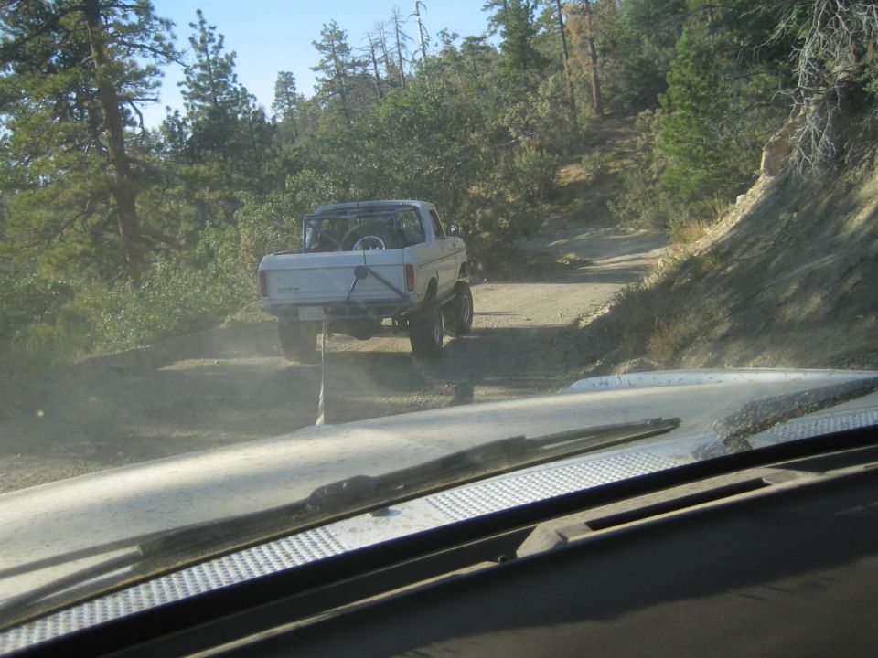 White lifted pickup truck climbing a dusty forest trail, seen through a windshield