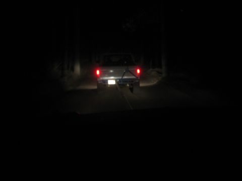 1990 Ford Bronco - Nighttime shot of a vehicle's glowing red taillights ahead on a dark wooded road, mostly black surroundings.