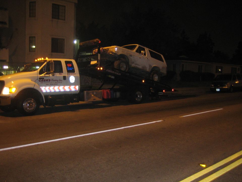 White SUV on a flatbed tow truck parked on a street at night