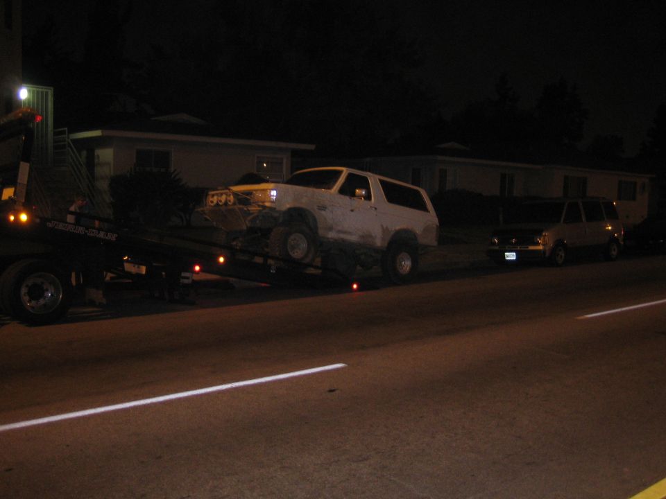 Muddy white SUV on a flatbed tow truck on a dark street at night