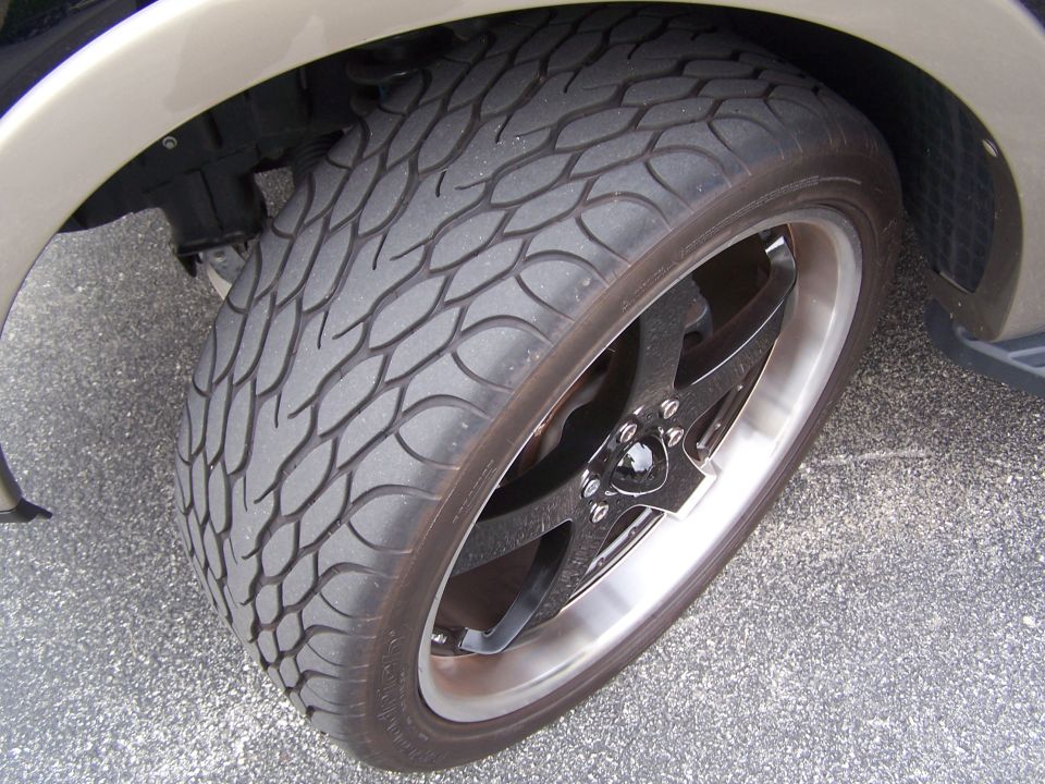 Close-up of wide low-profile tire on black five-spoke wheel with polished lip under tan truck fender