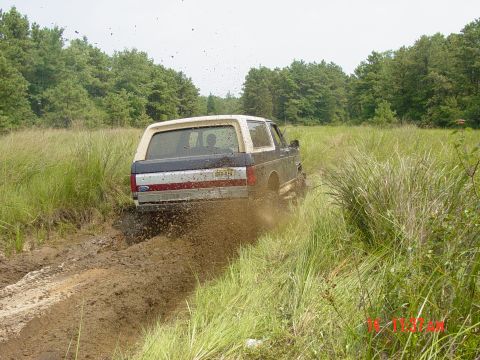 1995 Dodge 1500 - Ford Bronco navigating a muddy trail with mud spraying from the tires.