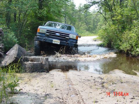 1995 Dodge 1500 - A blue Ford F-Series truck navigates a water obstacle on a dirt path.