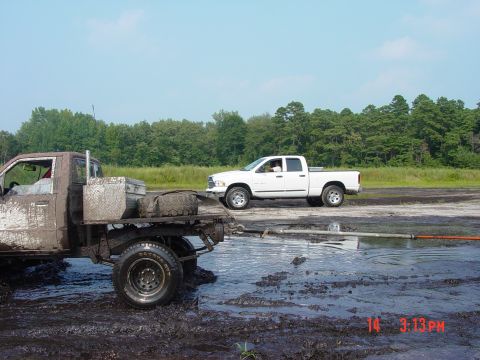 1995 Dodge 1500 - Two trucks are stuck in the mud on a sunny day with trees in the background.
