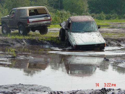 1995 Dodge 1500 - A Ford Bronco tows a pickup truck stuck in a muddy puddle.