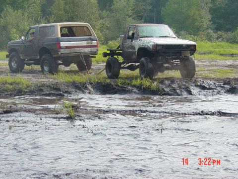 1995 Dodge 1500 - Two off-road trucks are stuck in a muddy area, with trees in the background.