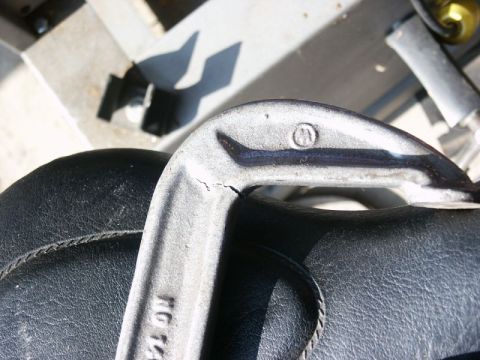 1996 Ford Bronco - A close-up view of a cracked metal component, possibly a lift part, situated on a black upholstered surface.
