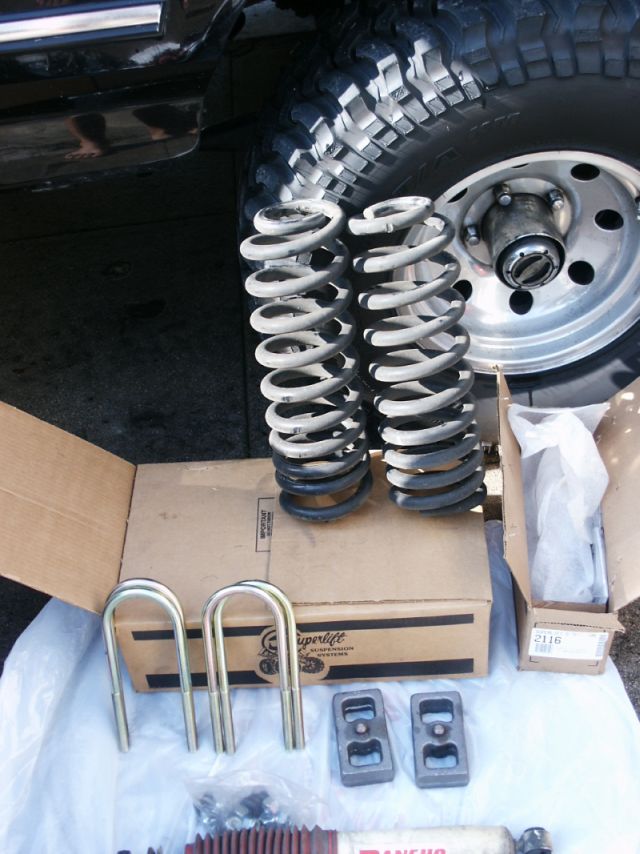 Suspension lift kit parts including coil springs, U-bolts, and blocks next to a vehicle tire