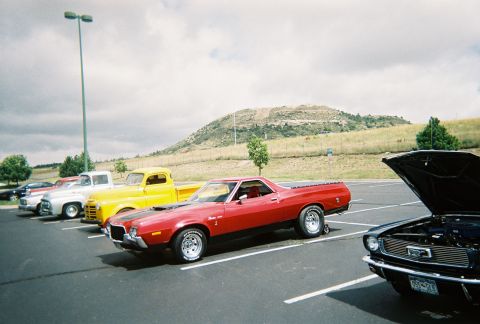 1972 Ford Ranchero - A row of classic vehicles, including a red 1972 Ford Ranchero, parked outdoors under a cloudy sky.