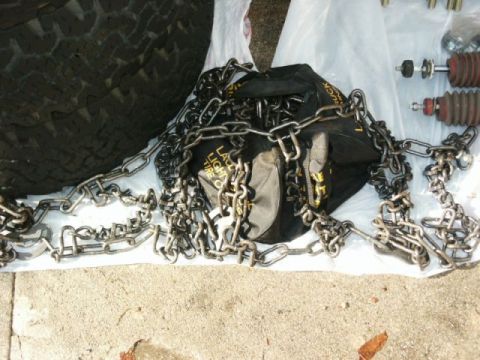 1996 Ford Bronco - Tire chains and shock absorbers are laid out on a concrete surface next to a tire.