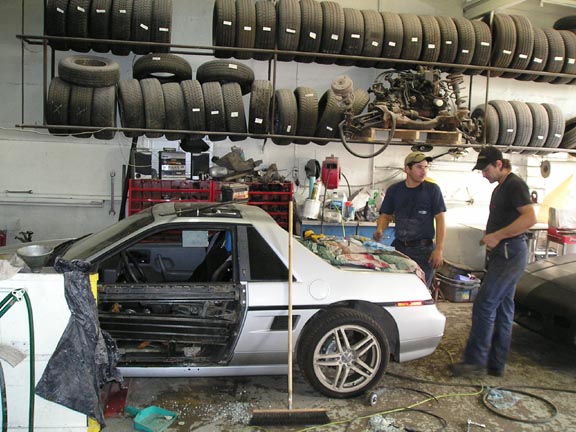 White 1984 Pontiac Fiero with door open, undergoing repairs