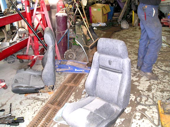 Two car seats, one in foreground, in a cluttered workshop with tools and equipment