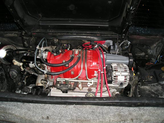 engine bay with red engine block, alternator, and spark plug wires