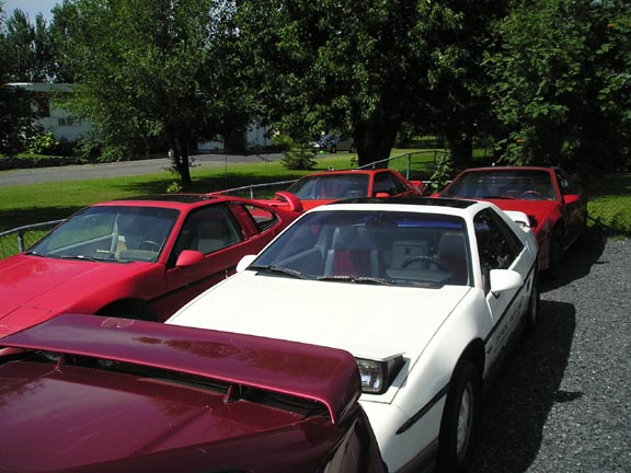White 1984 Pontiac Fiero parked with red Fieros behind it