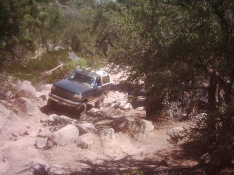 1978 Ford Bronco - A dark blue Ford Bronco navigates a challenging rocky trail with a white camper shell.