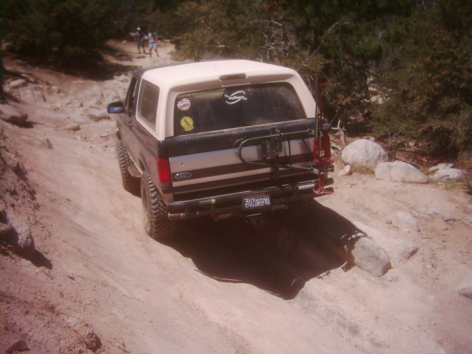 1990s Ford Bronco with a spare tire carrier and jack on a rocky dirt road