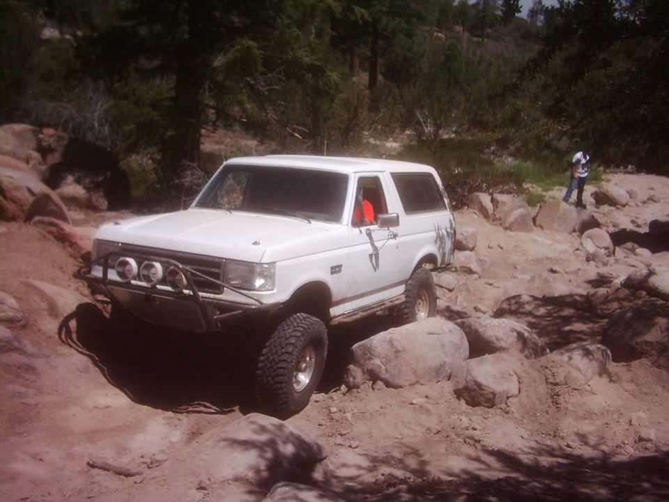 White Ford Bronco with aftermarket bumper and lights navigating a rocky trail
