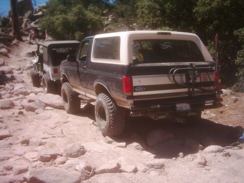 1978 Ford Bronco - A black and white Ford Bronco navigates a rocky off-road path, followed by another vehicle.
