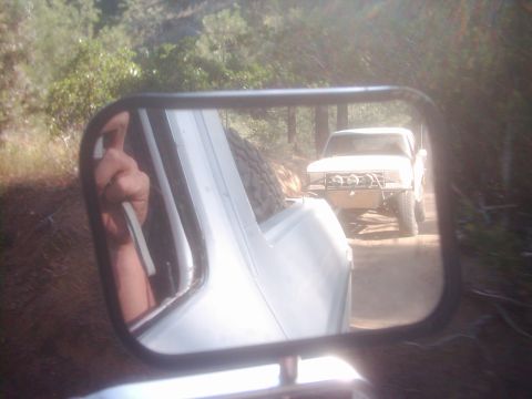 1978 Ford Bronco - Side mirror view of a white pickup truck driving on a dirt road.
