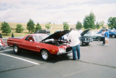 1972 Ford Ranchero - A red 1972 Ford Ranchero is parked with its hood up, while people examine the engine bay at an outdoor gathering.