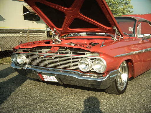 Red 1961 Chevrolet Impala with hood open, showing engine. Chrome grille and bumper