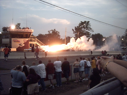 Drag race with large flame and smoke plume at New England Dragway, spectators watching