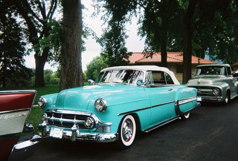 1972 Ford Ranchero - A turquoise 1954 convertible is parked in front of a silver pickup truck, with trees and a house in the background.