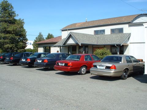 1999 Ford Crown Victoria - Multiple Ford Crown Victoria sedans are parked in a row outside a building on a sunny day.