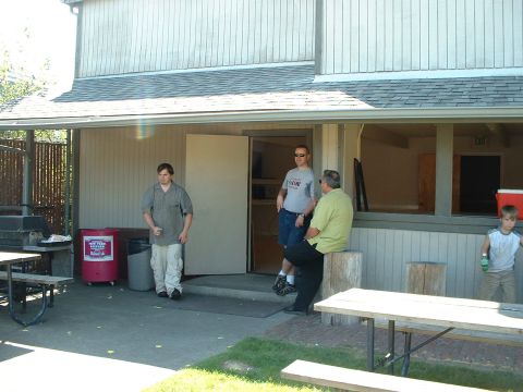 1999 Ford Crown Victoria - Several people are gathered outside a building on a sunny day, with picnic tables and a grill visible.