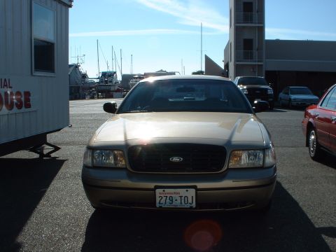1999 Ford Crown Victoria - Tan Ford Crown Victoria parked outdoors with other vehicles and a trailer nearby.