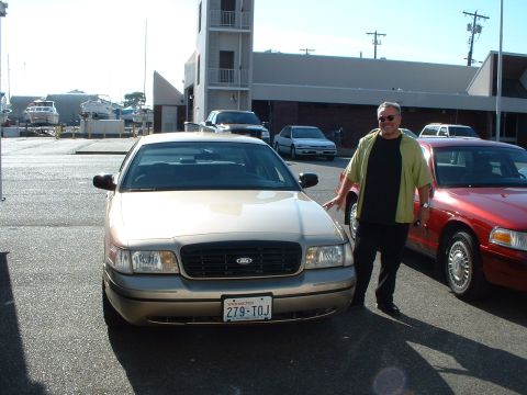 1999 Ford Crown Victoria - A man poses with a gold Ford Crown Victoria in a parking lot near a marina.