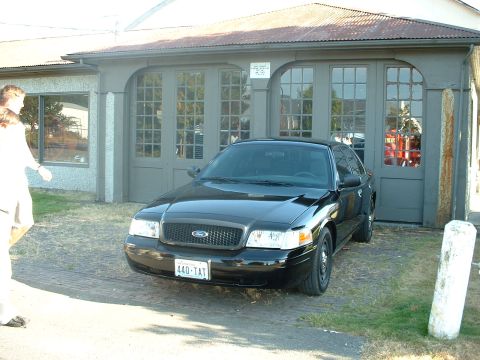 1999 Ford Crown Victoria - A black sedan is parked in front of a building with large, multi-paned doors.