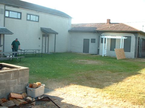 1999 Ford Crown Victoria - A man stands near picnic tables in a backyard area with buildings in the background.