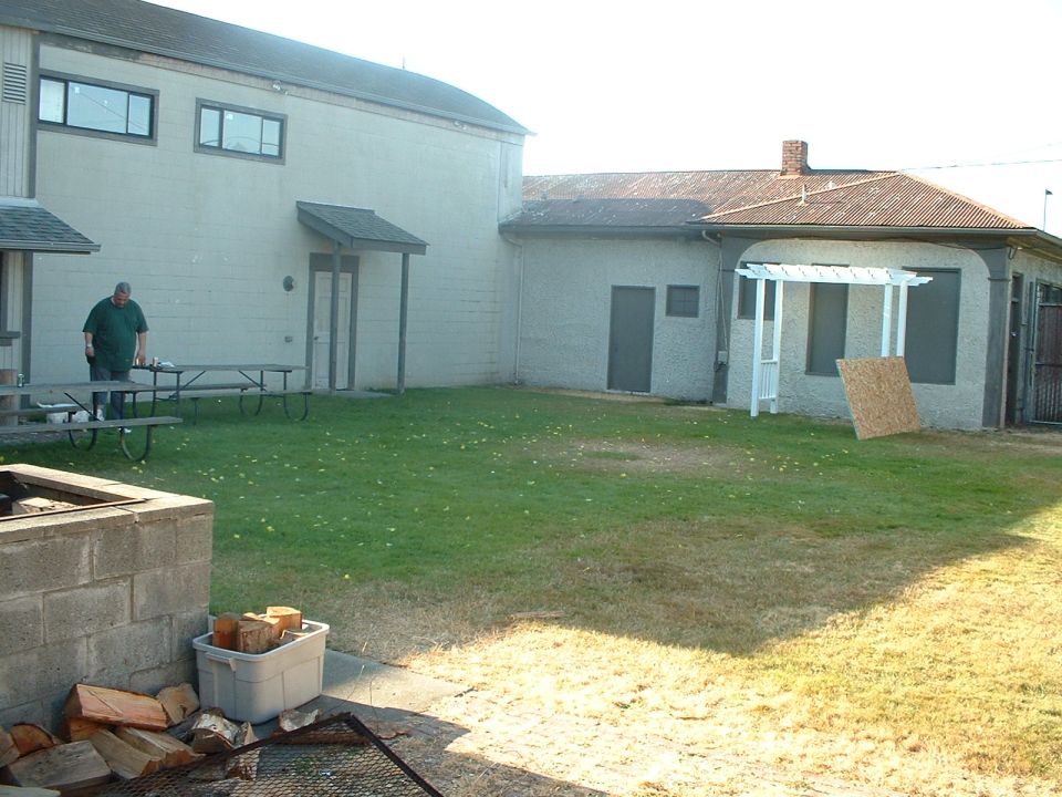 Man standing by picnic tables in a grassy yard next to a building