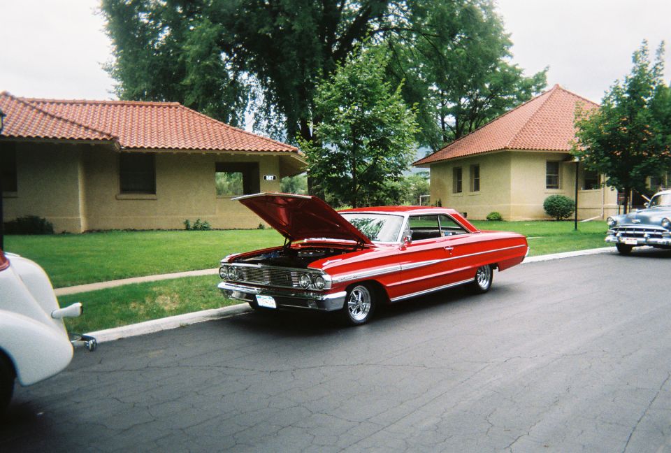 Red 1960s Ford two-door hardtop with hood up at a classic car gathering