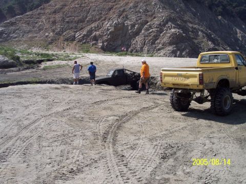 1985 Ford Bronco - Two trucks are stuck in the mud with people observing the situation.