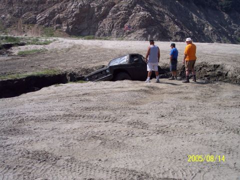 1985 Ford Bronco - A truck is stuck in a muddy ditch with three men observing the scene.