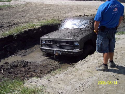1985 Ford Bronco - A muddy truck is stuck in a trench, with a person observing the scene.
