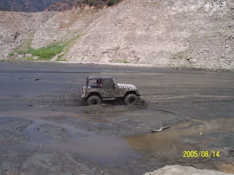 1985 Ford Bronco - A Jeep Wrangler navigates through a thick mud pit, kicking up spray.
