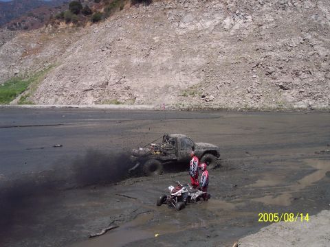 1985 Ford Bronco - Two off-road vehicles, a truck and an ATV, are stuck in the mud with one person on the ATV and two standing nearby.