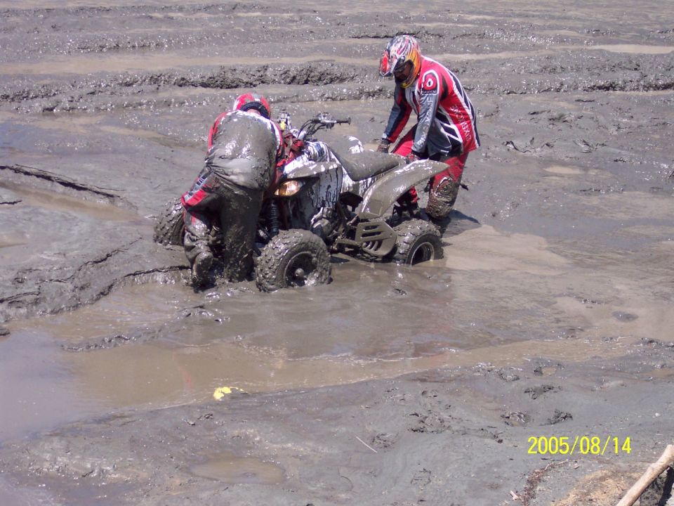 Quad bike stuck in mud with two riders in red and black gear