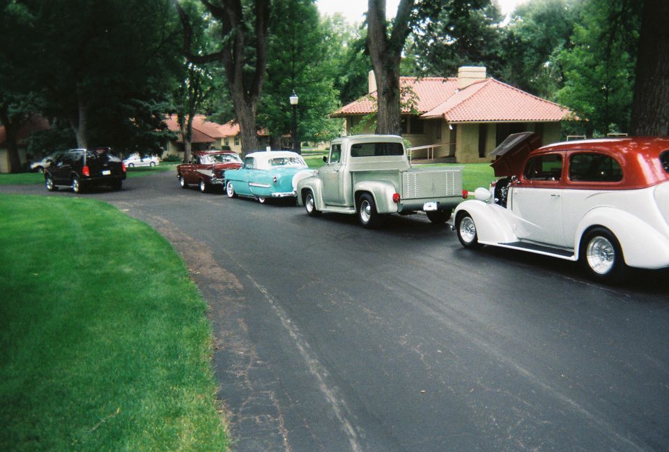 Row of classic cars and trucks parked along a park drive at a car show